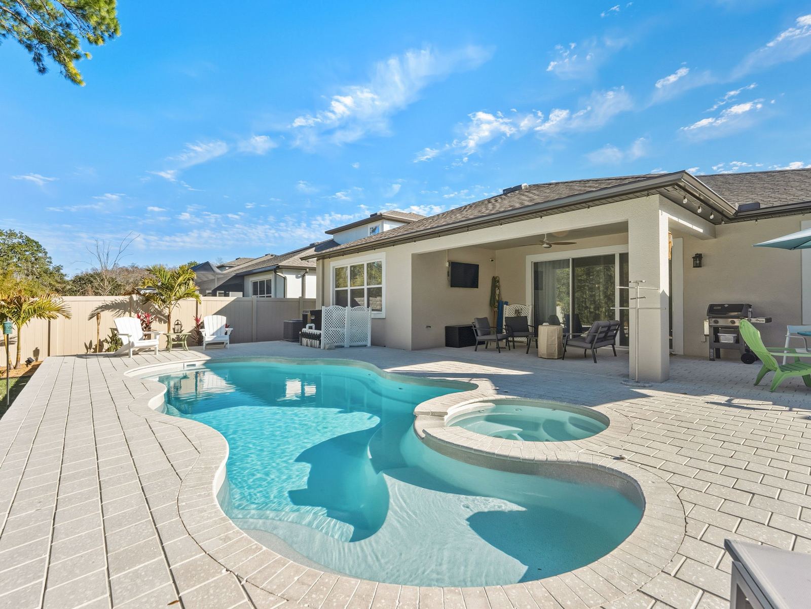 Freeform fiberglass pool with a sun shelf and attached spa on a white paver deck