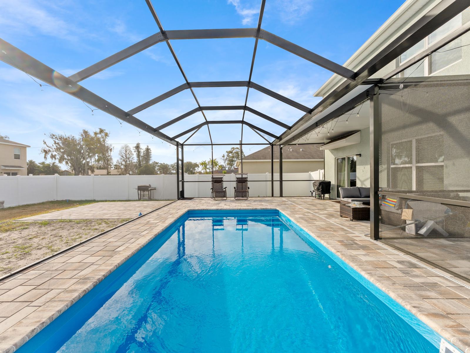 Long rectangular fiberglass pool with a sun shelf inside a screened enclosure