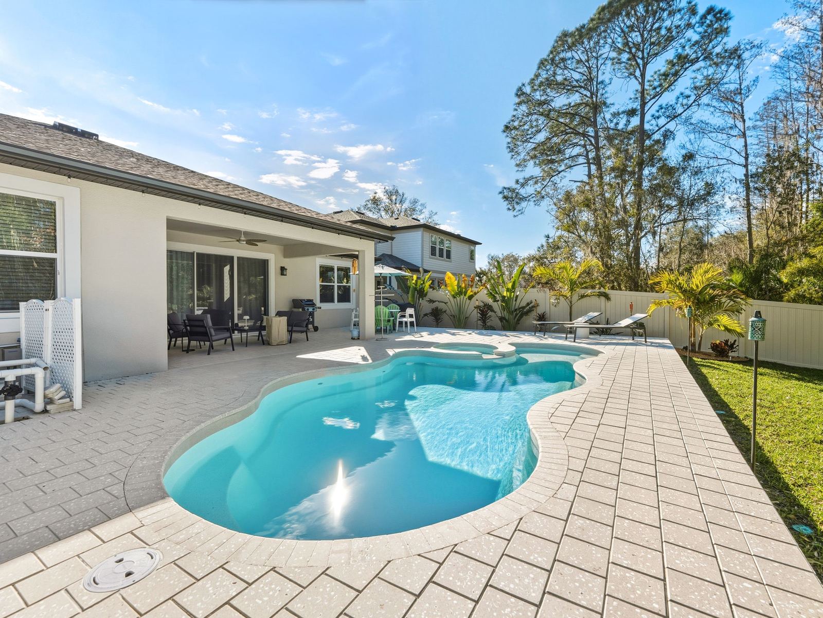 Freeform fiberglass pool along a white paver deck beside the house