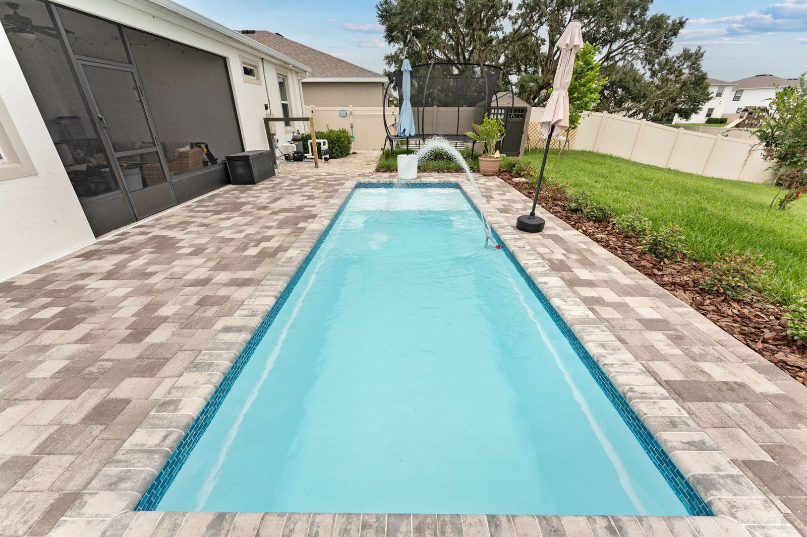Narrow lap-style fiberglass pool with a deck jet and paver deck